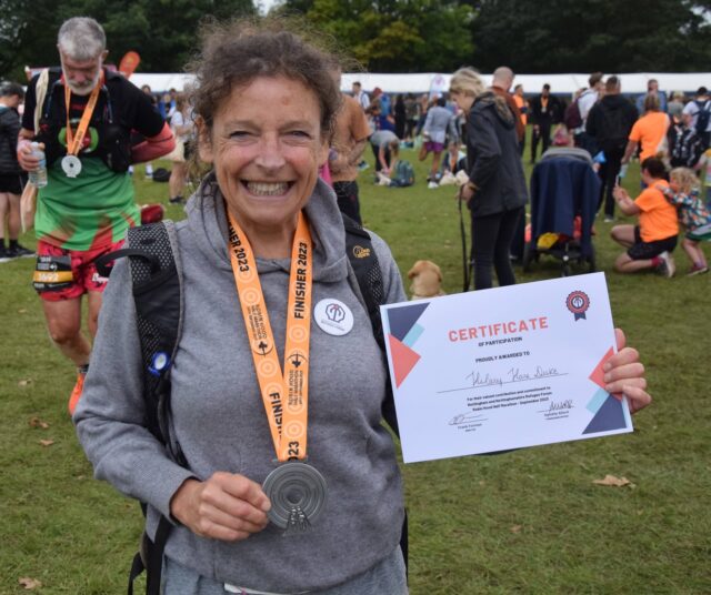 Runner holding medal and certificate saying thank you for running the robin hood half and fundraising for the forum